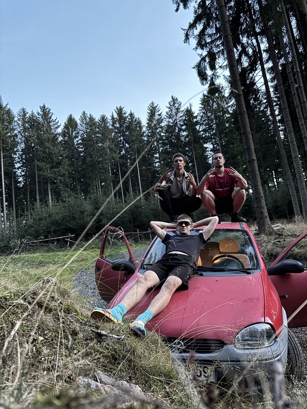 Tři kamarádi u červeného auta v lese